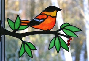 stained glass baltimore oriole on a window frame metal branch with red berries